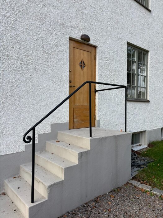 Trappa och dörr med enkel putsad fasad från ett hus byggt runt 1914-18. Dörren har en dekorativ rutform i trä och svart trappräcke.
