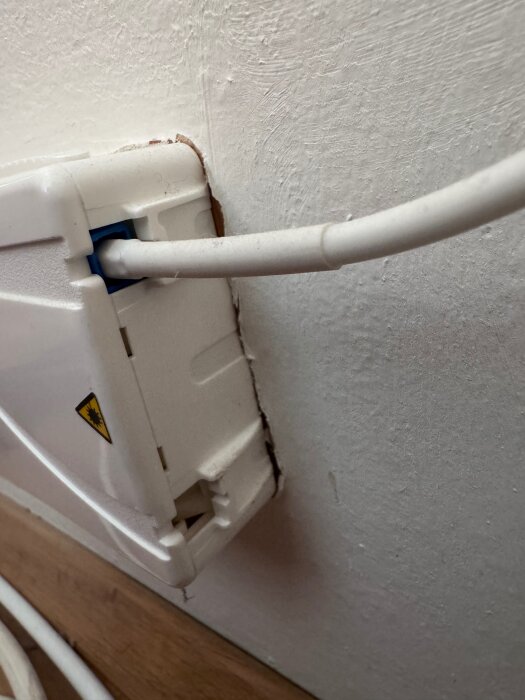 En vit kabelbox på en vägg med sladdar som kommer ut från sidan, visar var skruvarna för att ta bort boxen kan sitta fast.