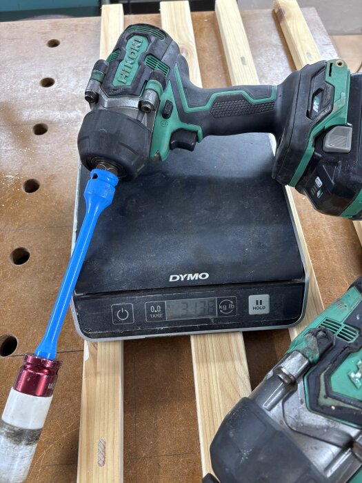 En batteridriven mutterdragare med ett blått fäste ligger på en digital våg som visar vikten 3,13 kg.