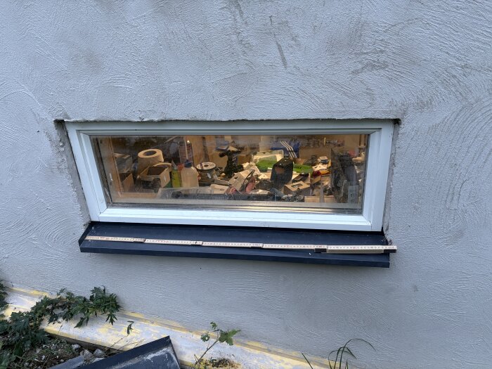 Fönster i en putsad fasad med svart bleck och linjal; byggmaterial syns inuti huset. Tråd om putsning kring fönster och överbleck.