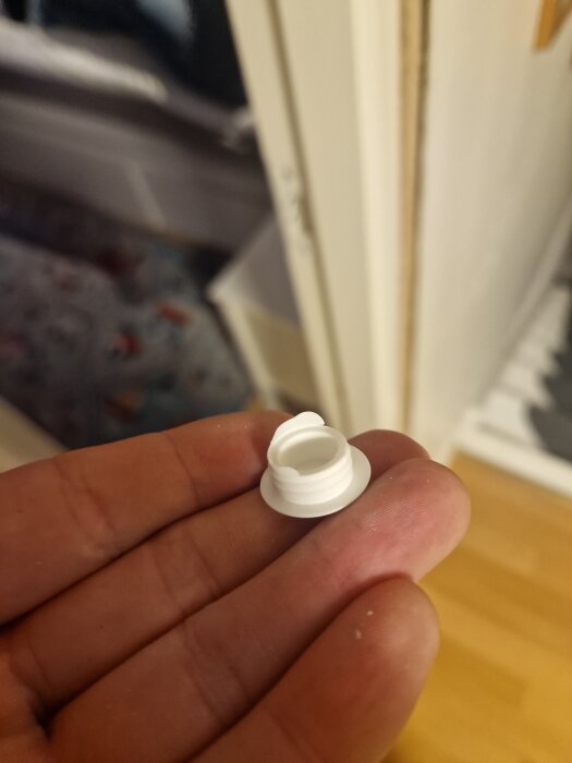 Vit plastplugg hålls i en hand framför en dörr som inte går att stänga ordentligt.