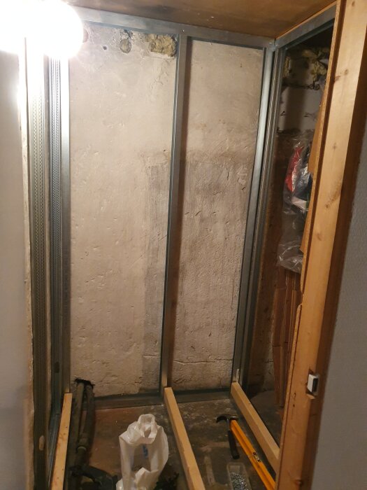 Reglar och väggkonstruktion i en källare under renovering, med verktyg och material på golvet.