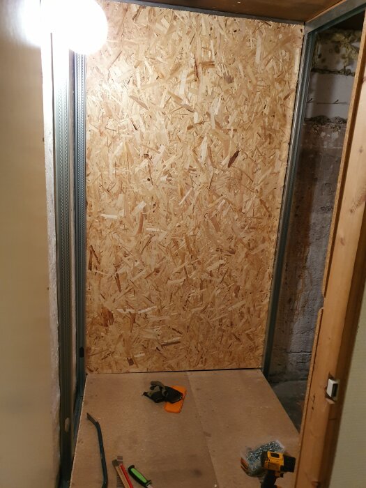 OSB-skiva monterad på vägg i ett mindre källarrum under renovering, verktyg och material ligger på golvet i förgrunden.