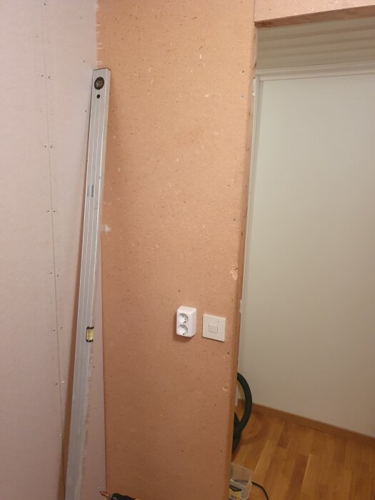 Källarvägg under renovering med osynlig dörrkonstruktion; vattenpass och elkontakt synliga på väggen.