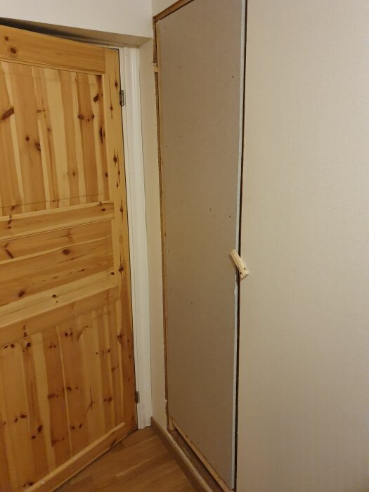 Väggkonstruktion i trä och gipsskiva bredvid en trädörr, del av projekt för hemligt rum med dolda ingångar och dold stenväggsdörr för vinkällare.