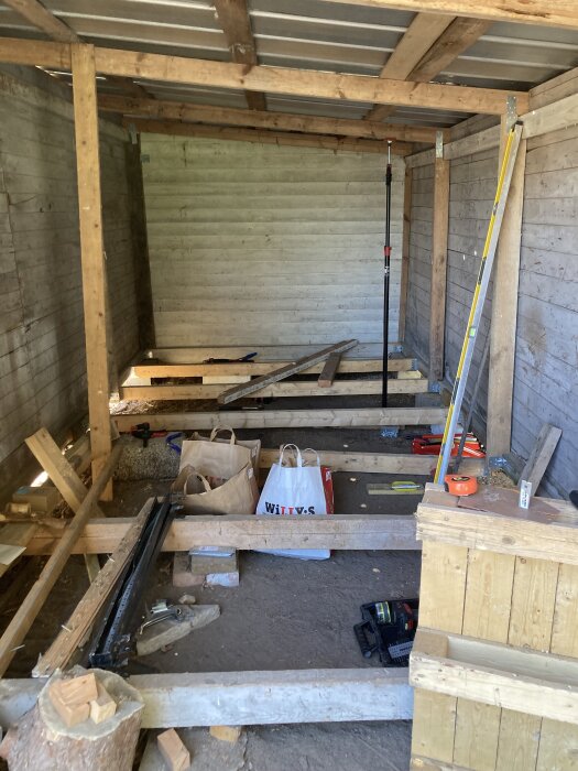 Vedbod under renovering, med träreglar, verktyg och byggmaterial spridda på golvet.