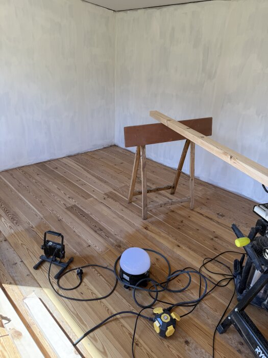 Renovering i rum med nytt återbrukat trägolv, såg och elverktyg synliga på golvet, vita väggar.