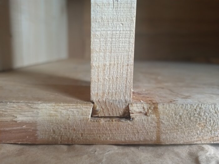 Trädetalj med skadad limning och skruvhål, del av en kommod under renovering. Fokus på gradspåret där en trasig list suttit monterad.