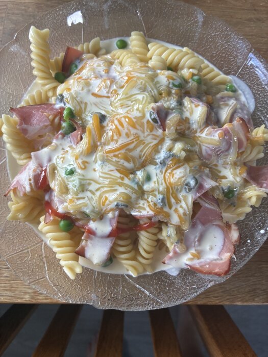 Gräddstuvad pasta med skinka, cheddar, mozzarella, kapris, gröna ärtor och italienska kryddor på klar tallrik.