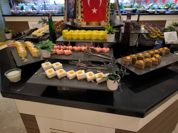 Olika bakverk på buffébord, inklusive färgglada tårtbitar och smårätter, dekorerade med grädde och frukt.