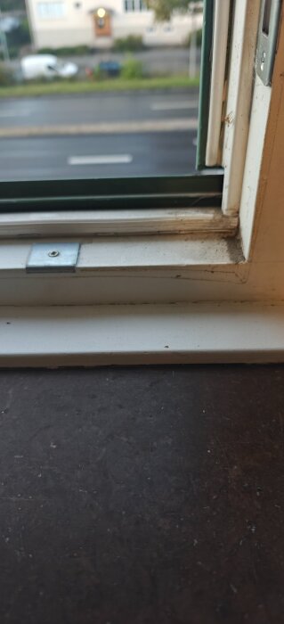 Fönsterkarm med smuts, utsikt över gata och hus i bakgrunden.