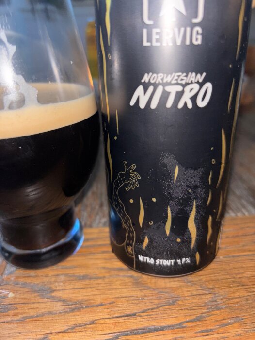 Burk med Lervig Norwegian Nitro stout bredvid ett glas fyllt med skummande öl på ett träbord.