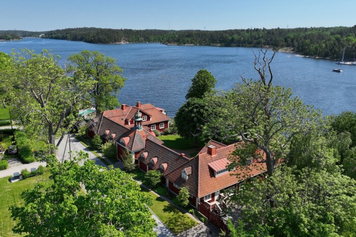 Röda hus med tegeltak vid vattnet, omgivna av grönskande träd i Saltsjö-Duvnäs, Nacka.