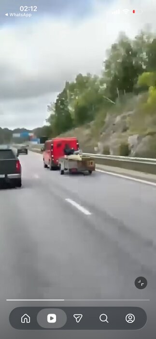 En röd bil drar ett släp med fastsurrade plankor på en motorväg.
