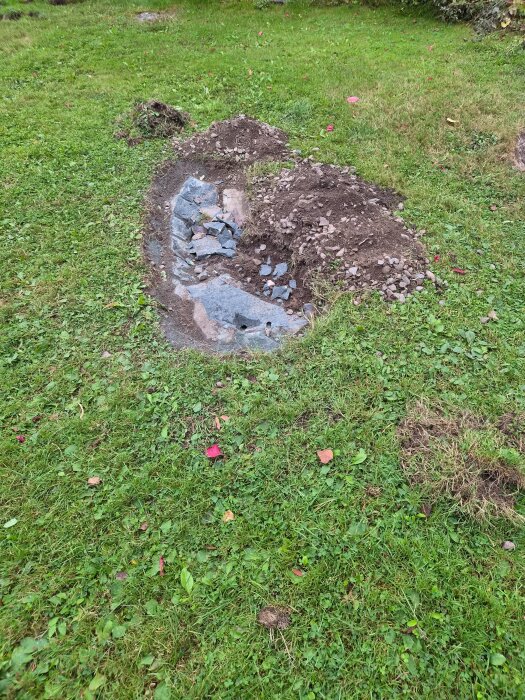 Markyta med utspridd jord och sten ovanpå gräs, troligen del av ett pågående grävarbete eller trädgårdsprojekt.
