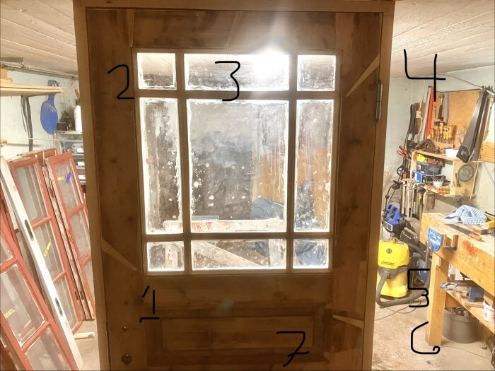 Gammal träport med glasrutor, siffror markerade på ramarna, ljus från glödlampa ovan. Verktyg och material synligt på arbetsbänkar i bakgrunden.