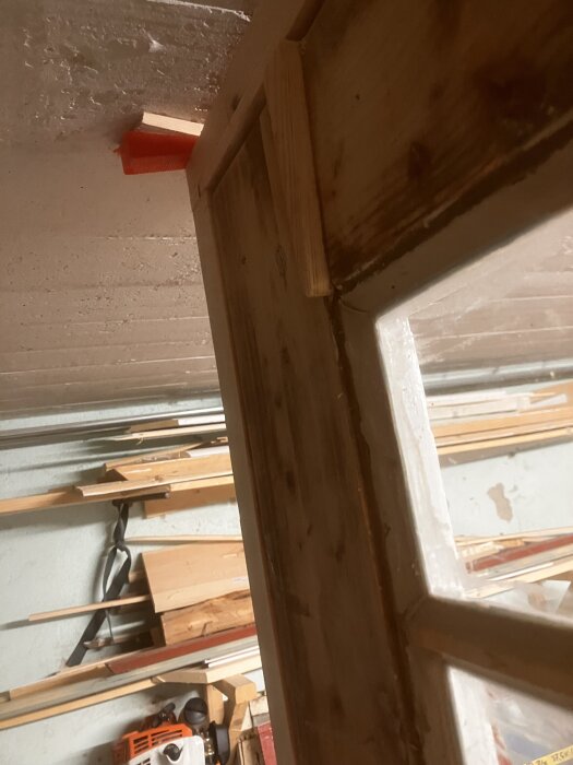 Träram i ett byggprojekt, provisoriskt kilad i taket med en orange plastkil och träbitar. Bakom syns träverktyg och trästycken på väggen.