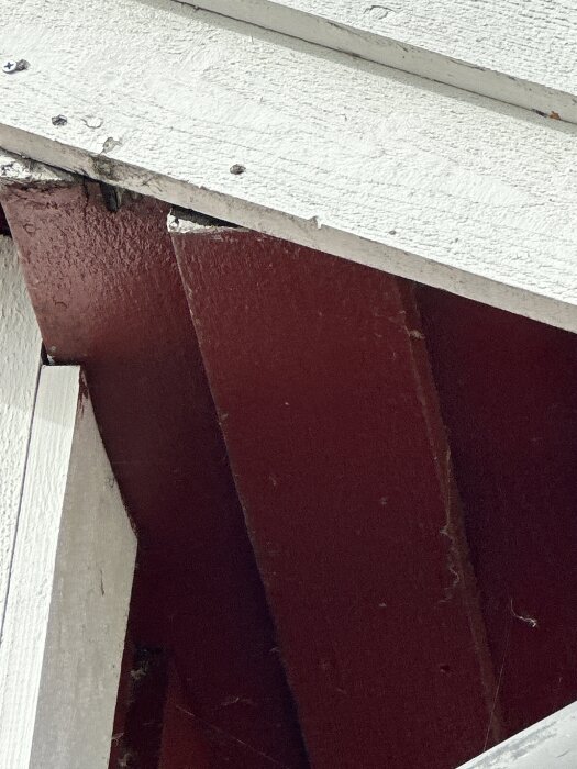 Närbild av röd träpanel med vita trädetaljer och några synliga skruvar.