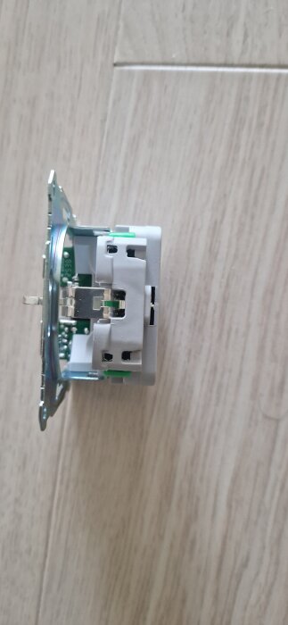 Vägguttag med USB-ingångar och gröna snabbkopplingsspakar, sett från sidan på ett ljust träunderlag.