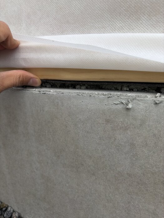 Hand håller byggplast och träsyll vid betongplatta, visar glapp mellan syll och platta.