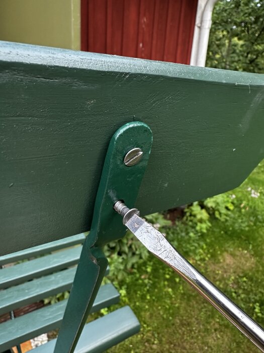 Grön trädgårdsstol i metall, stor skruvmejsel drar åt en skruv i stolens stomme, grönmålad yta.