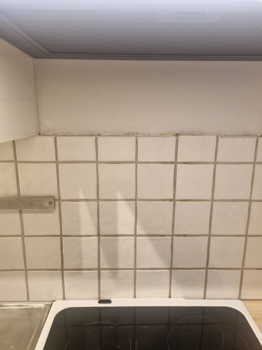 Ojämn kant på kakel vid spishäll med nyligen installerad köksfläkt ovanför.