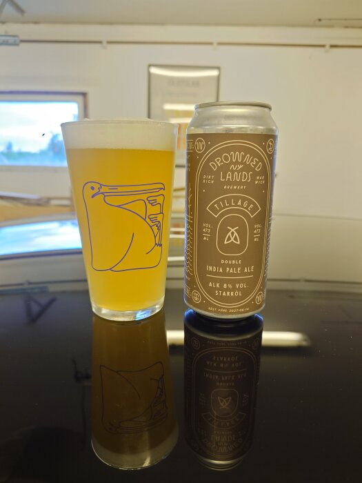 En burk Drowned Lands India Pale Ale bredvid ett glas med öl mot en reflekterande yta.