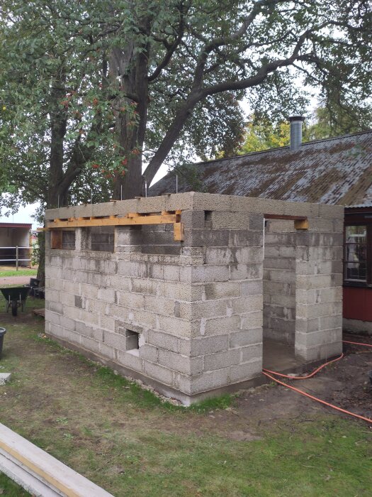 Byggnad med betongblock och förstärkt balk under konstruktion, omgiven av träd.