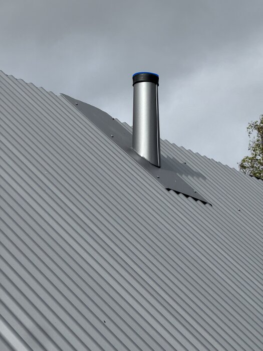 Plåtbeklädd skorsten på ett tak av korrugerad metall under en grå himmel.