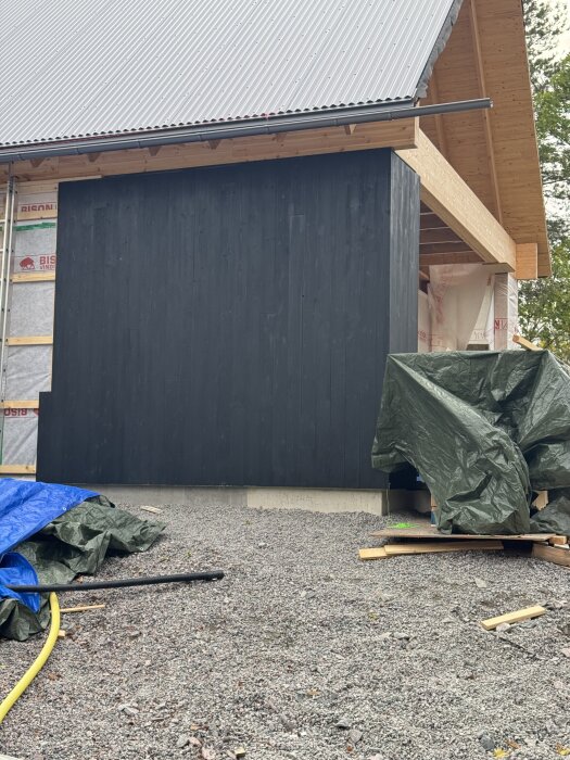 Byggprojekt med svartmålad fasad och nytt plåttak, arbete pågår. Anpassningar vid fönster och dörröppningar syns.