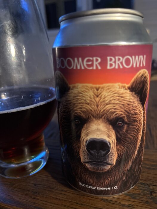 Burk med Boomer Brown Ale och ett glas öl på ett träbord.