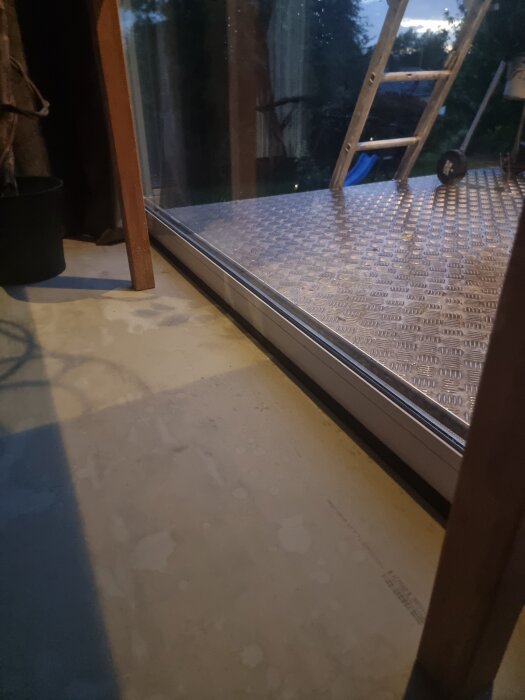 Stora fönsterpartier med synlig läcka vid karm och båge där vatten tränger in. Utsikt mot altan och stege syns utanför.