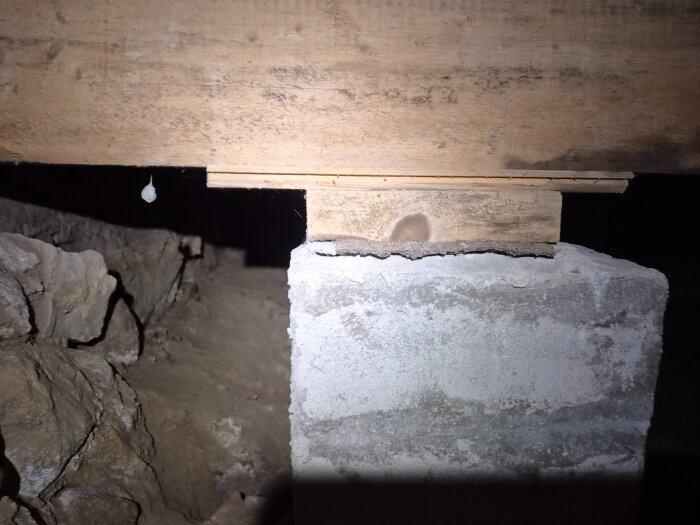 Betongpelare som stödjer en träbalk i en krypgrund. Balken visar tecken på fukt och röta.