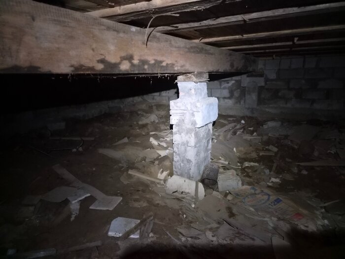 Krypgrund med fukt och rötskador, en träbalk bärs upp av en stenstolpe. Golvbjälkar och spill syns på marken.