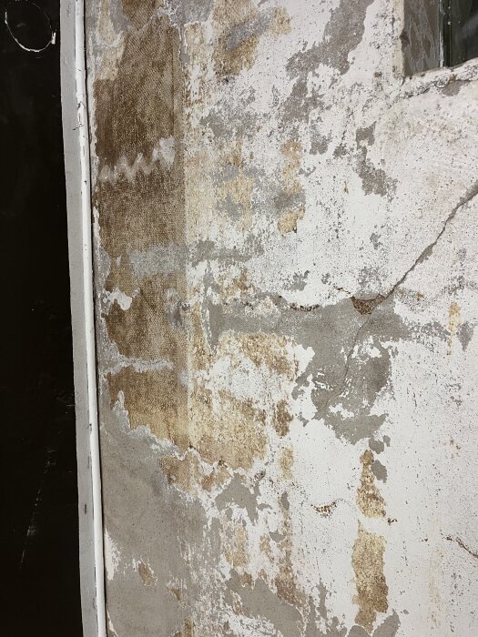 Källarvägg med rester av panel och väv, fläckar på betongen visar kvarvarande färgspår efter borttagning och skrapning.