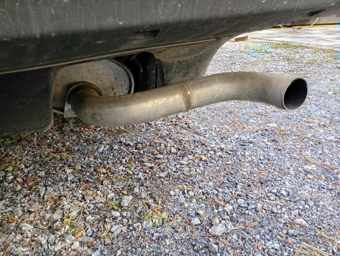 Avgasröret på en bil, sett bakifrån. Lyftas mot en grusbelagd yta under bilen, delen är ny med rostfläckar runt omkring.
