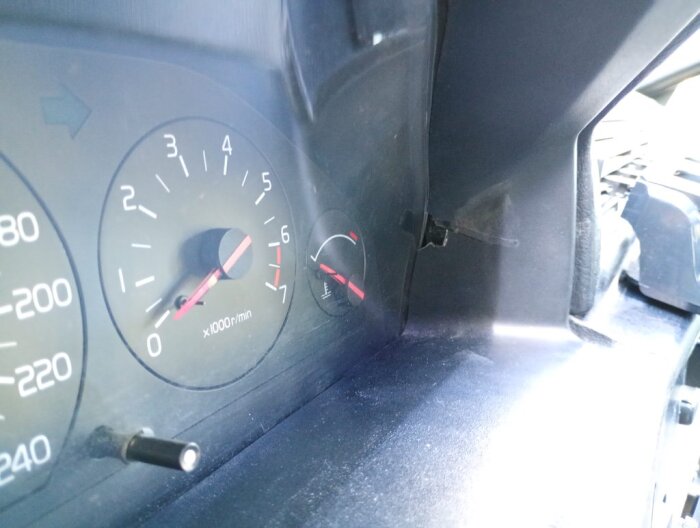 Instrumentpanelen på en äldre Volvo, visar en varvräknare och en temperaturmätare. Det finns en spricka i plasten bredvid mätarna.