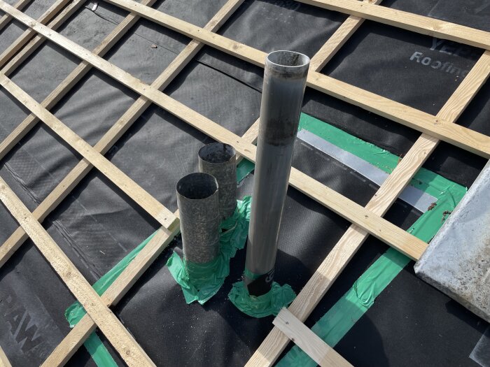 Tre ventrör på ett tak, två mindre och ett större, täckta med grönt tejp runt basen, omgivna av råspont och takpapp.