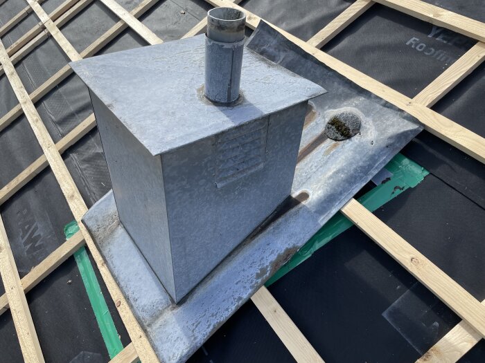 Ojämnt monterad ventilationshuv i plåt på tak, orsakar kondensproblem. Huven täcker ventiler och luftningsrör, potentiellt utan isolering.