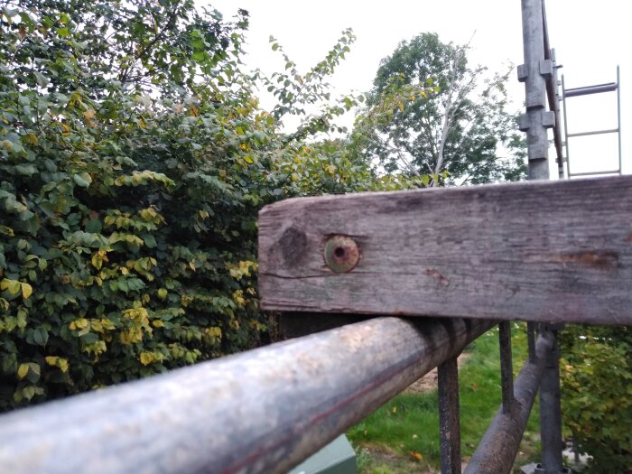 Träställning med invändig gänga och metallrör, utomhusmiljö med grönska i bakgrunden.