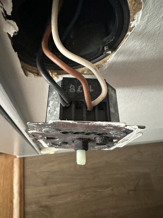 Gammal dimmer med två svarta, en brun och en vit ledare anslutna, inbyggd i en väggdosa med träbakgrund.