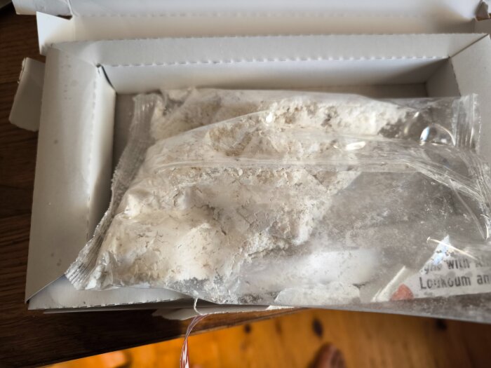 En öppen kartong visar en plastpåse med vitt pulver och några kubformade gelégodisar.