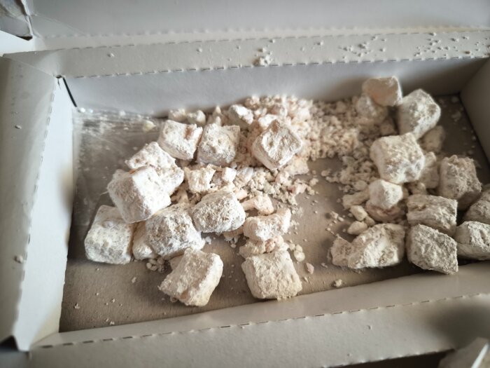 Kubformade godisbitar täckta med vitt pulver ligger i en öppen kartong, vilket verkar vara turkiskt godis av typen lokum.