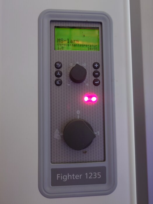 Kontrollpanel för värmepump med display som visar "MS-larm" och temperatur, med knappar och rattar. Märke: Fighter 1235.