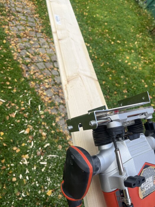 Handöverfräs från Black & Decker används för att bearbeta en träplanka, omgiven av gräsmatta och stenar med fallna löv i bakgrunden.