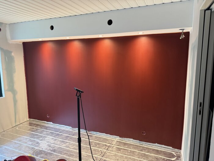 En rödvägg i ett sovrum med integrerad belysning ovanför; golvet är täckt för skydd under renovering.