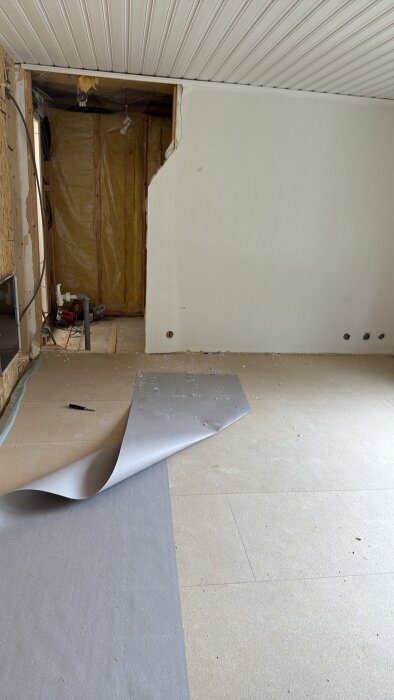 Vägg öppnad för renovering med synlig isolering och hål i gips, del av tak och golv syns med en uppvikt matta.