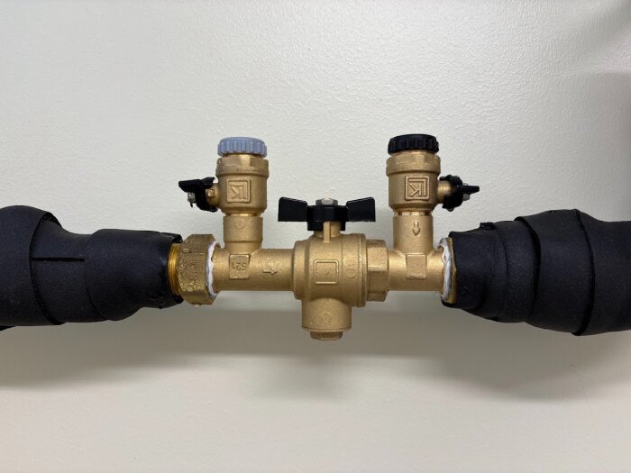 Ventilinstallation med två kranar, svart och grå, ansluten till isolerade rör. En pil visar vätskeflödesriktning. Möjligtvis felsatt rör på pumpen.