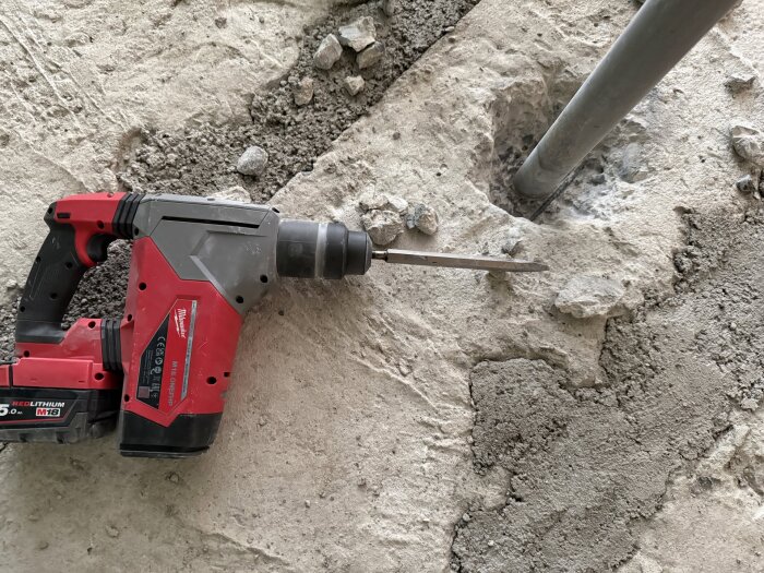 Borrmaskin och hål i betonggolv, bredvid ett metallrör, under en renovering av badrum.