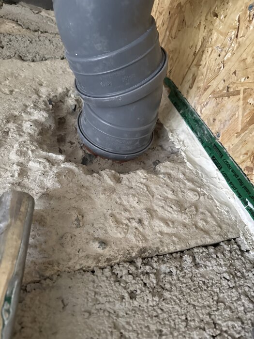 Avloppsrör av PVC i betonggolv med grönt tätningsband vid isolerat träregelverk i byggprojekt.